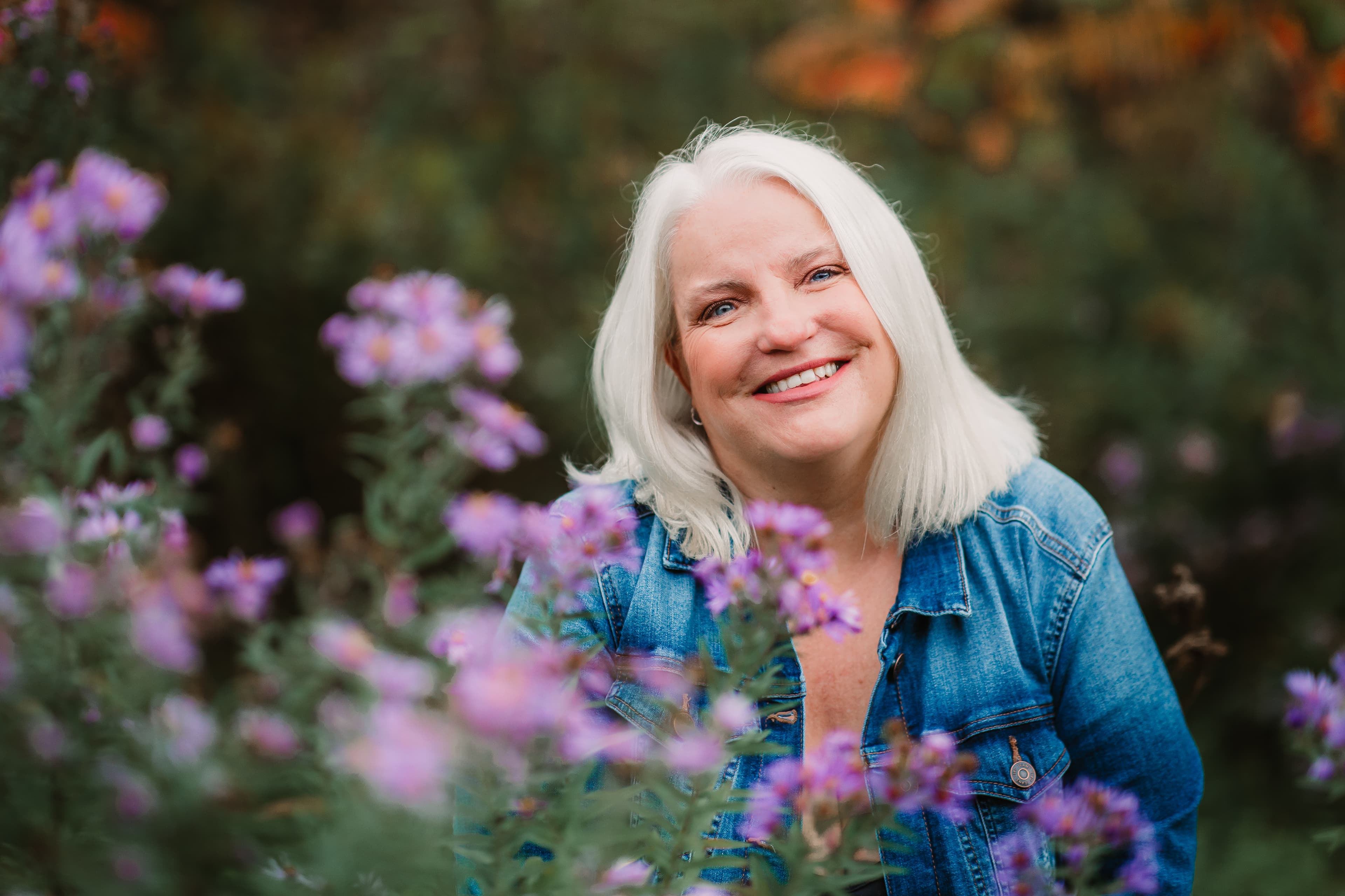 Nola Simon smiling among purple wildflowers in a denim jacket
