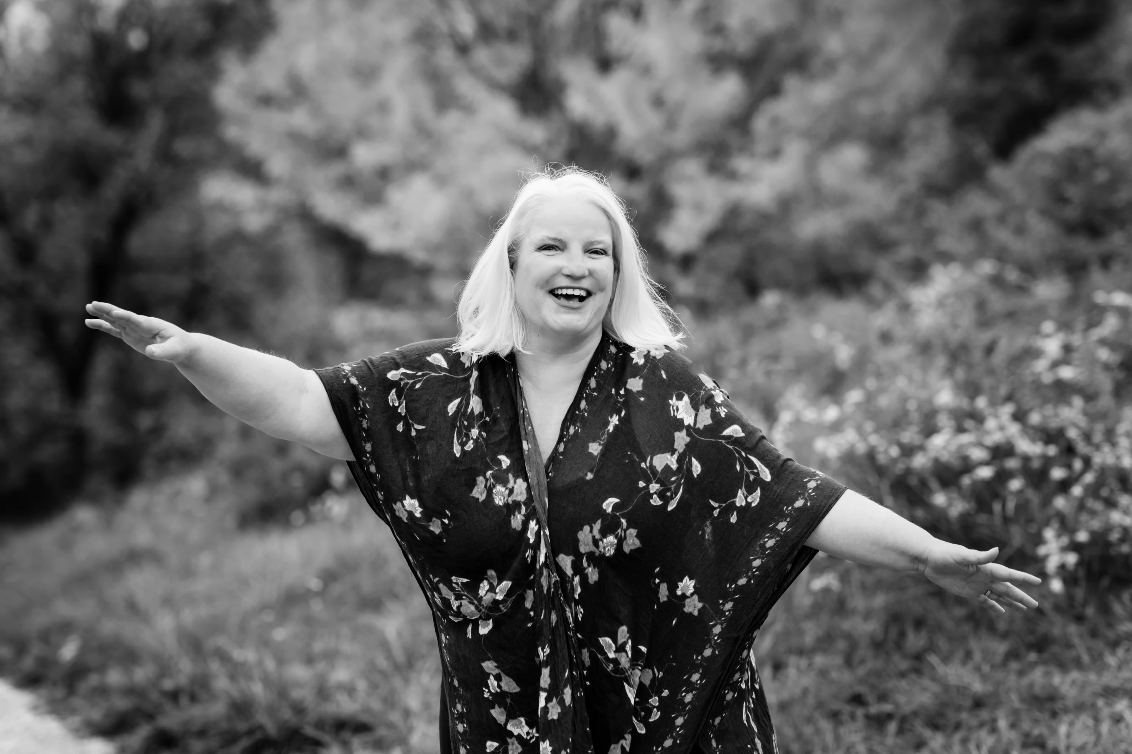 Nola Simon with arms open wide, laughing joyfully — black and white